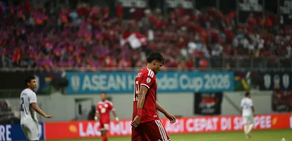 Jugador con camiseta roja caminando cabizbajo en el campo