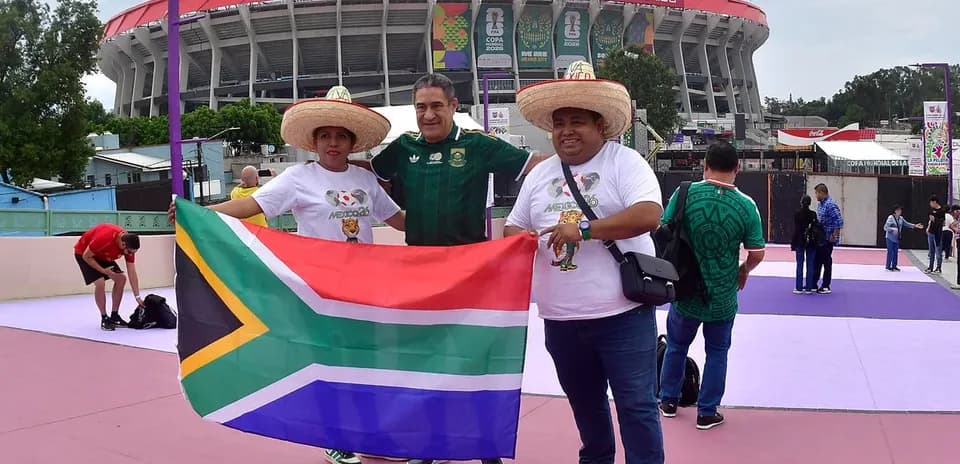 Tres aficionados sosteniendo bandera de Sudáfrica en estadio