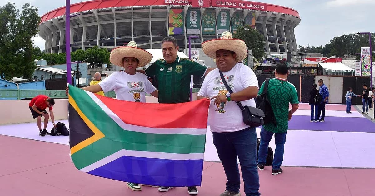 Tres aficionados sosteniendo bandera de Sudáfrica en estadio