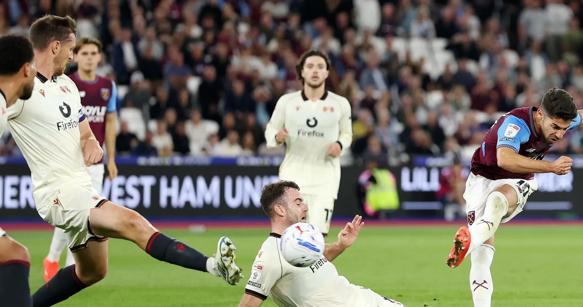 Jugador de West Ham disparando mientras rival cae al suelo