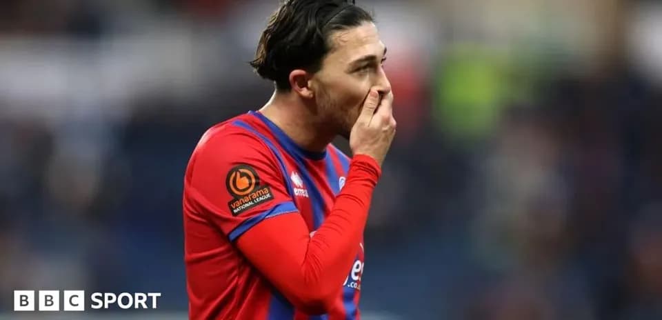 Jugador con camiseta roja tocándose la boca en el campo