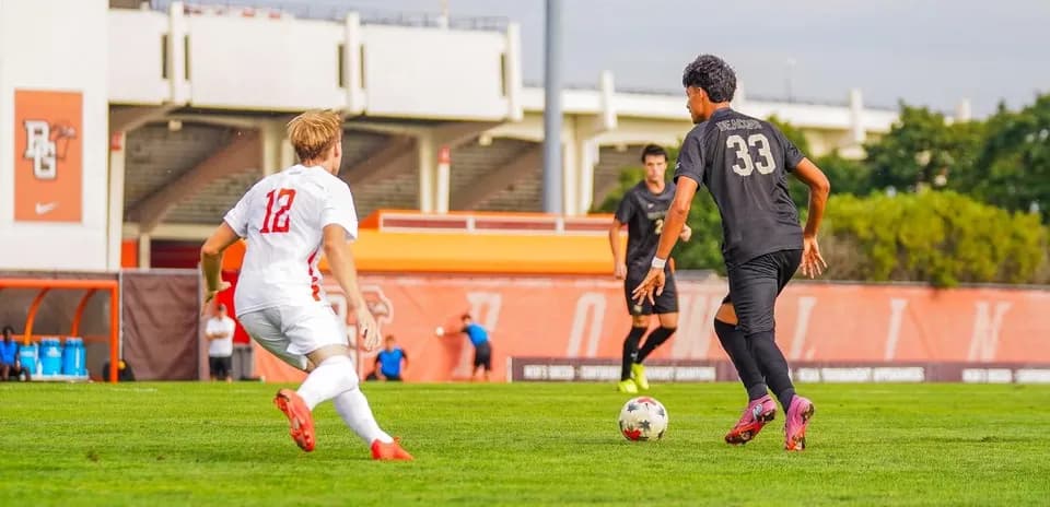 Jugador con balón y rival en campo de fútbol