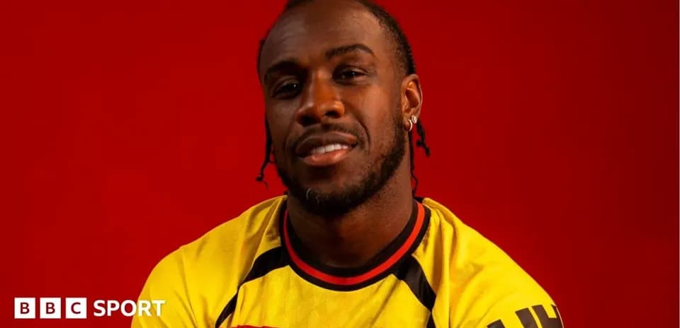 Jugador posando con camiseta de Watford frente fondo rojo