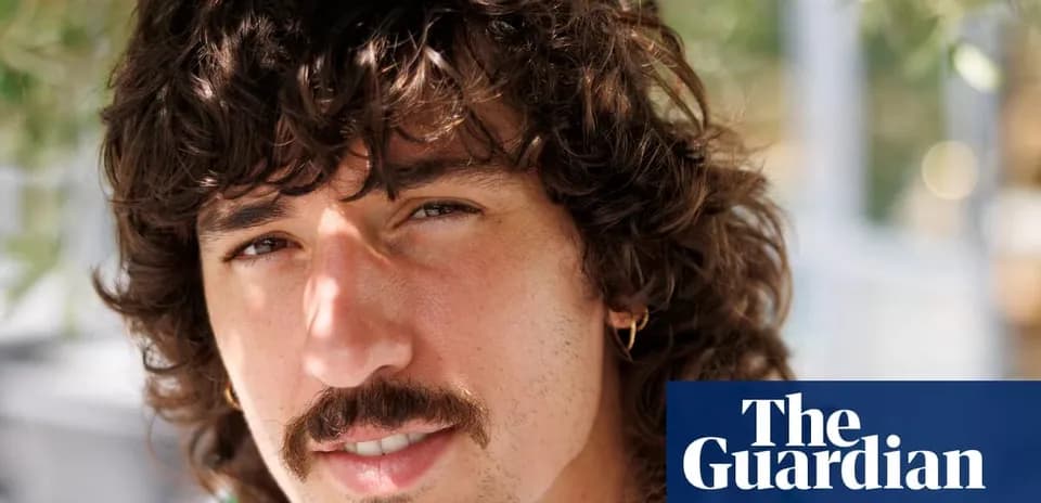 Hombre con cabello rizado y bigote, sonriendo