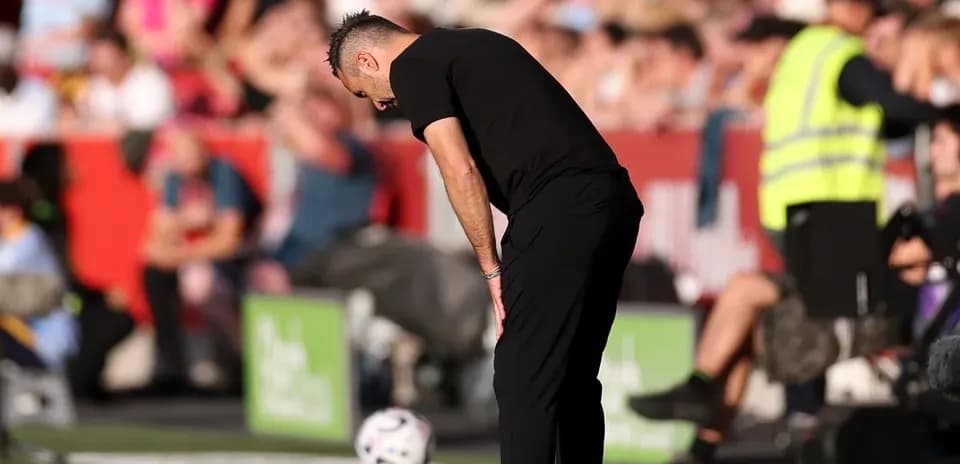 Entrenador agachado junto a balón en la línea lateral